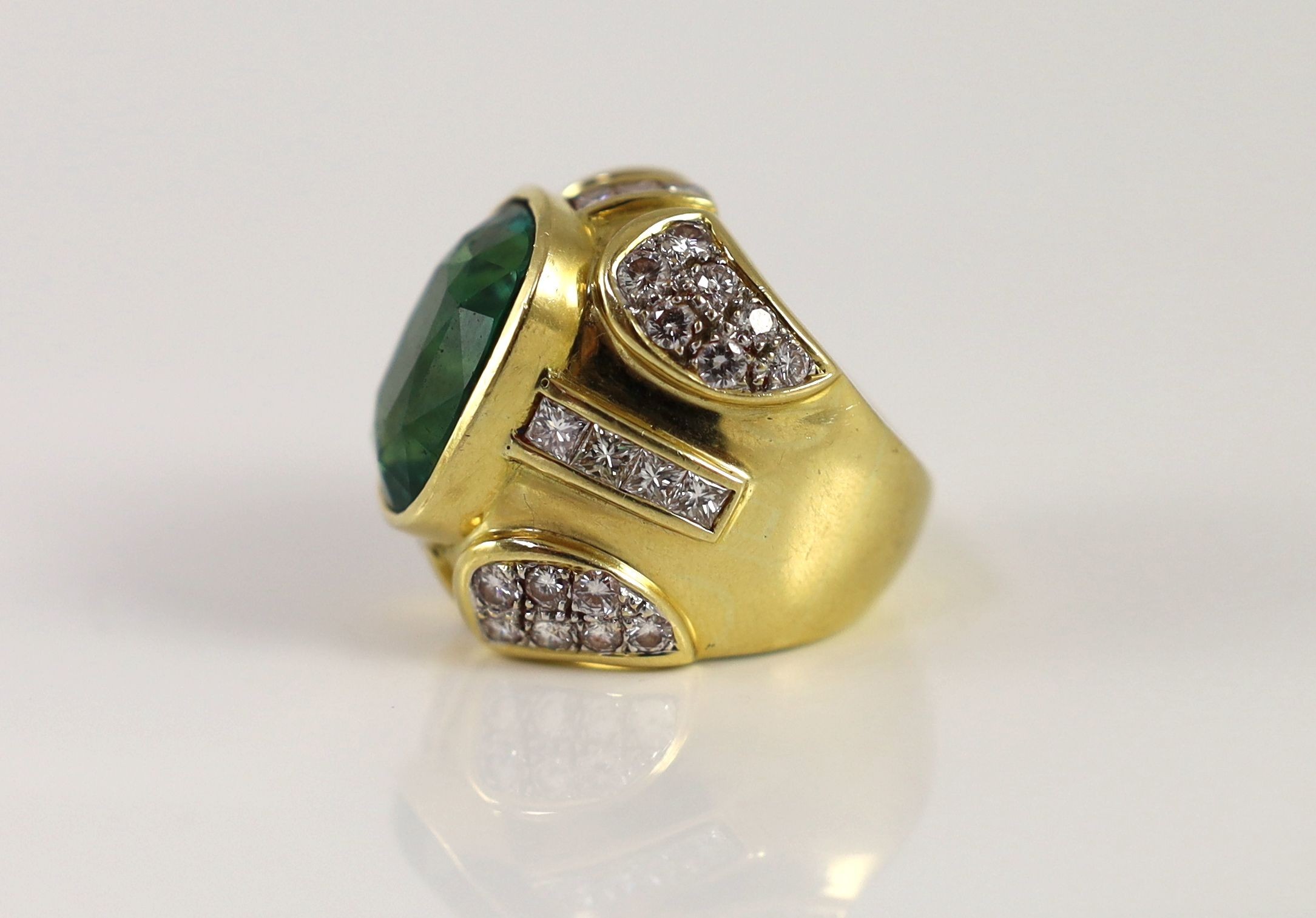 A large gold and single stone oval cut emerald set dress ring, with round and princess cut diamond cluster set shoulders